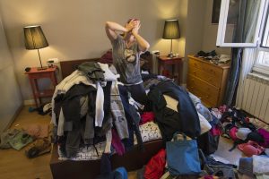 Portrait of woman crying among tiles of clothes in a messy bedroom