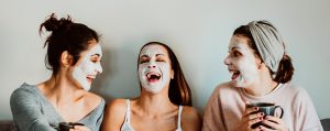 Cheerful Women With Facial Mask Sitting On Sofa At Home