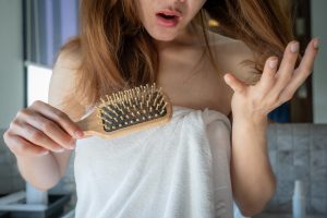 Close-up of worried woman holding comb with hair loss after brushing her hair.
