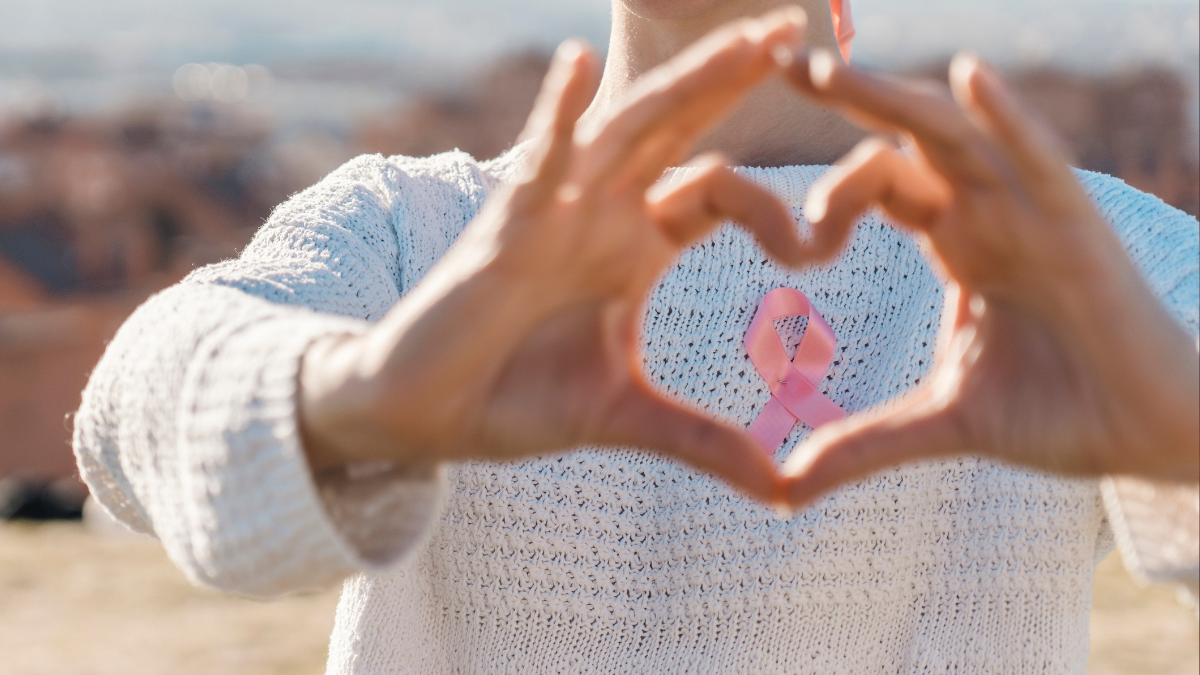Mujer haciendo un corazón con sus manos, mientras usa la cinta que apoya el cáncer de mamá. | Crédito: Getty images.